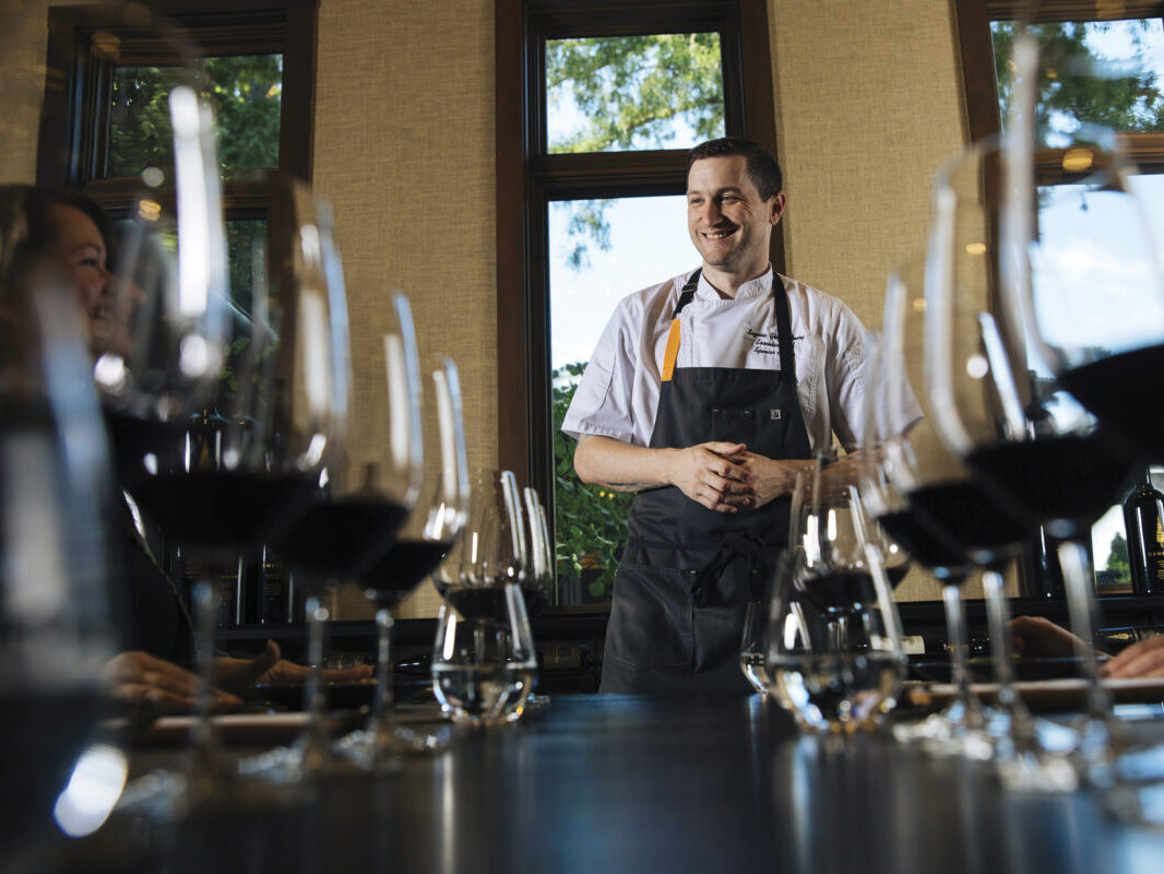 Sequoia Grove Executive Winery Chef Spencer Conaty standing at end of table with wine glasses with red wine set up for tasting, smiling