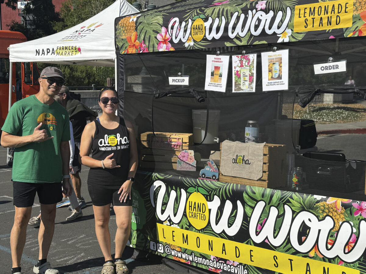 man and woman standing in front of lemonade stand, smiling