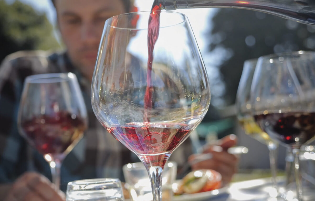 man looking at glasses of red wine in foreground