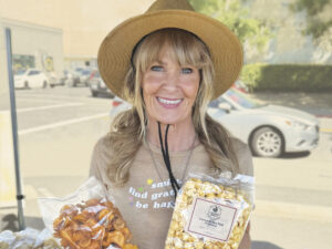 woman under tent wearing straw hat, holding bags of popcorn, smiling