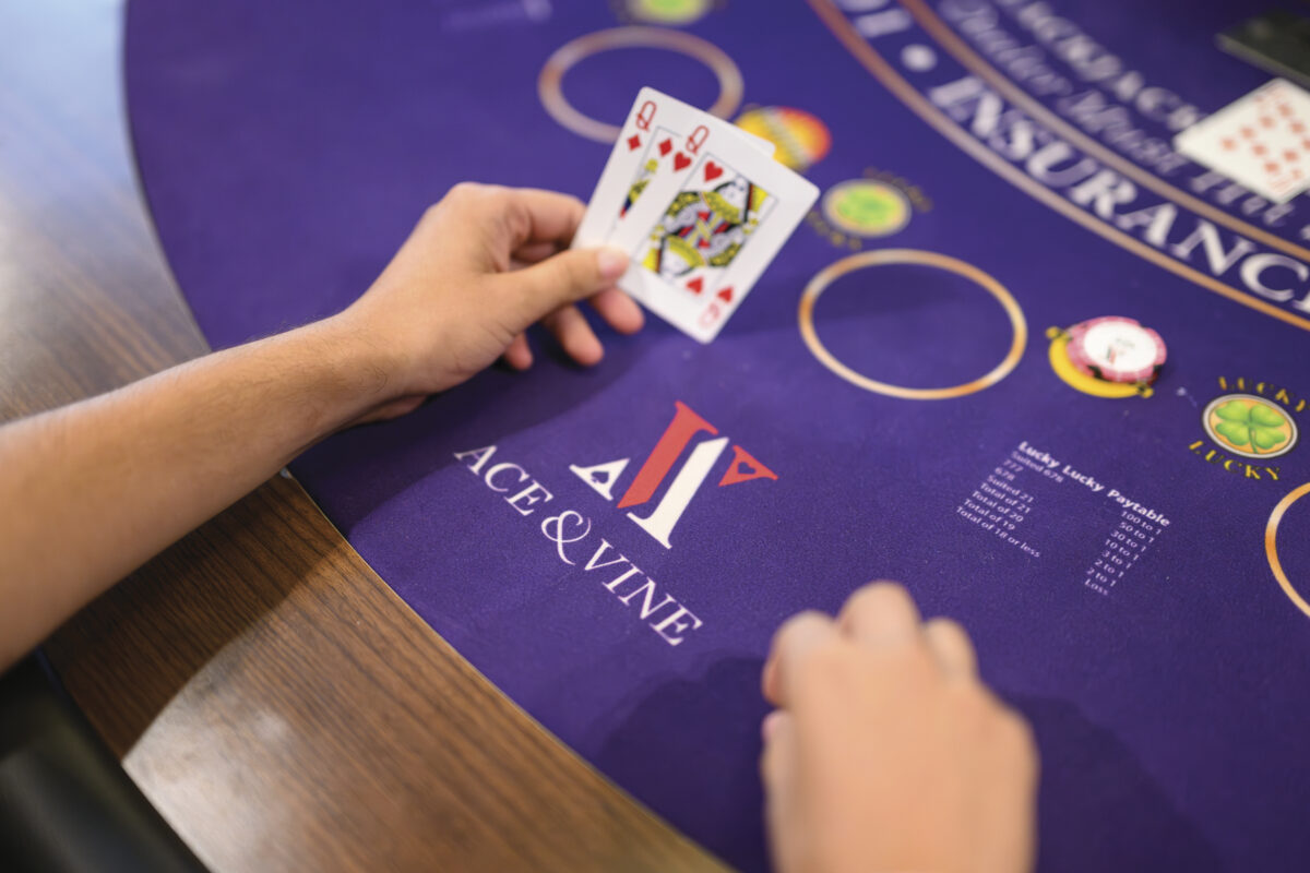 person holding 2 cards at poker table with purple felt for the article Late Night Napa