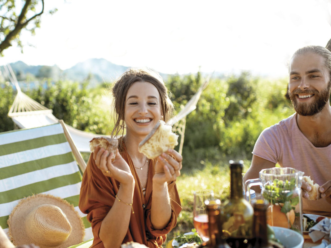 Young and cheerful woman having festive lunch at the beautifully decorated table with healthy food in the garden