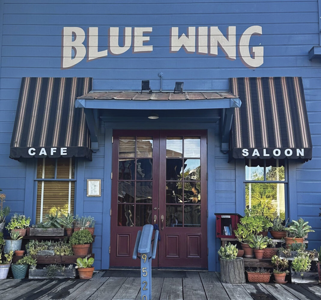 entrance of Blue Wing Saloon in Upper Lake with striped awnings over windows and "Blue Wing" painted on blue building