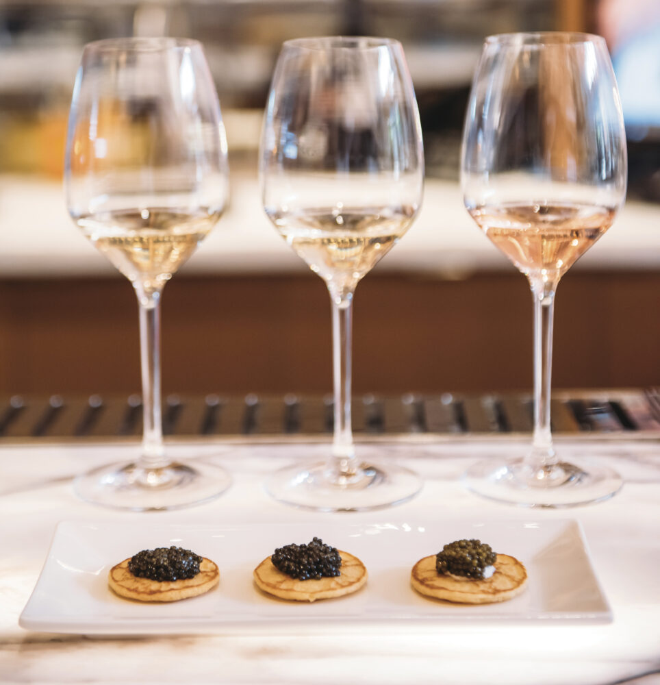 3 glasses of wine and plate with 3 crackers with caviers set up for tasting for the article Amuse Bouche