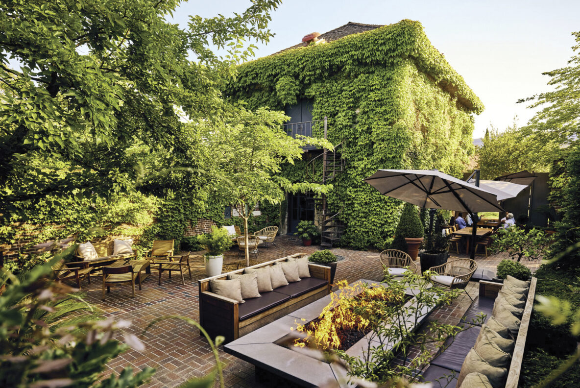 exterior view of Charter Oak with firepit and outdoor furniture, umbrellas and vines growing on the building in the background for the article Taking Off The Chill 