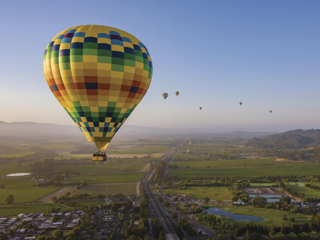 colorful hot air balloons in flight over Napa Valley with blue sky for the article Yountville