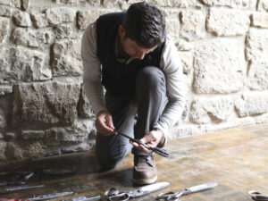 Dave Phinney of Orwin Swift kneeling looking at vintage scissors on wood floor with stone wall. For the article on Cult Winemaker Dave Phinney