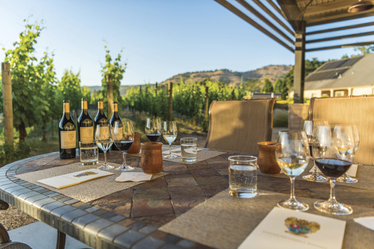 covered outdoor table set with menus, bottles of wine, glasses and winery in background