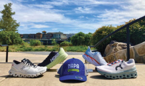 outdoor display of running shoes and hat with the words "Napa Running Company" on it with blue sky and park in background 