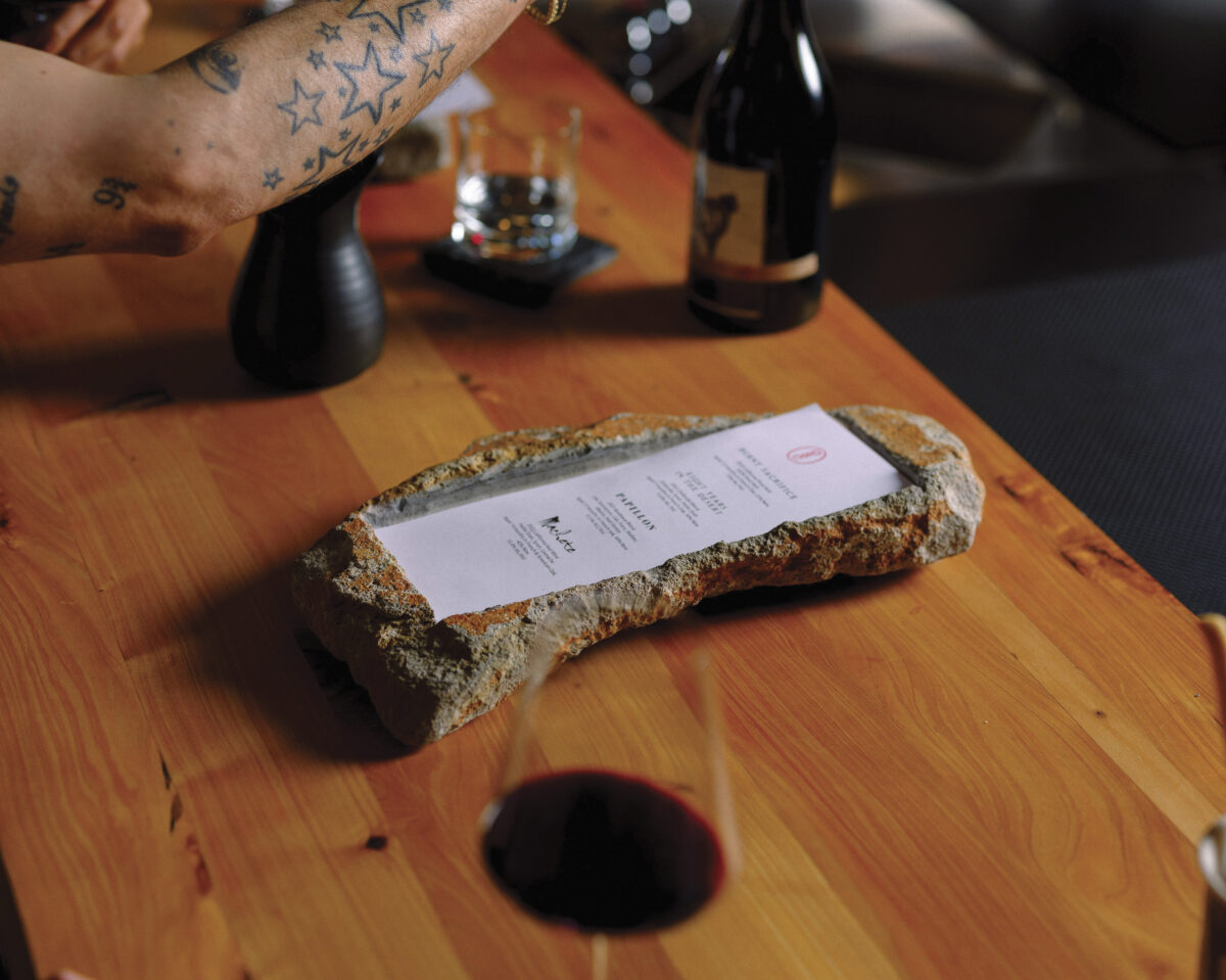 menu displayed on rock on wood table with wine bottle and glass for the article Cult Winemaker Dave Phinney