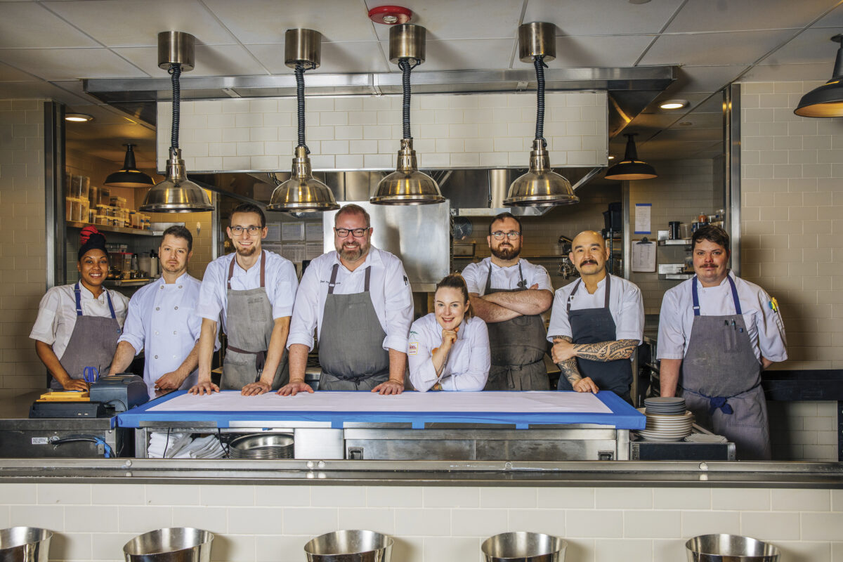 Chef Thomas Lents and the Violetto team wearing gray aprons in the kitchen, smiling