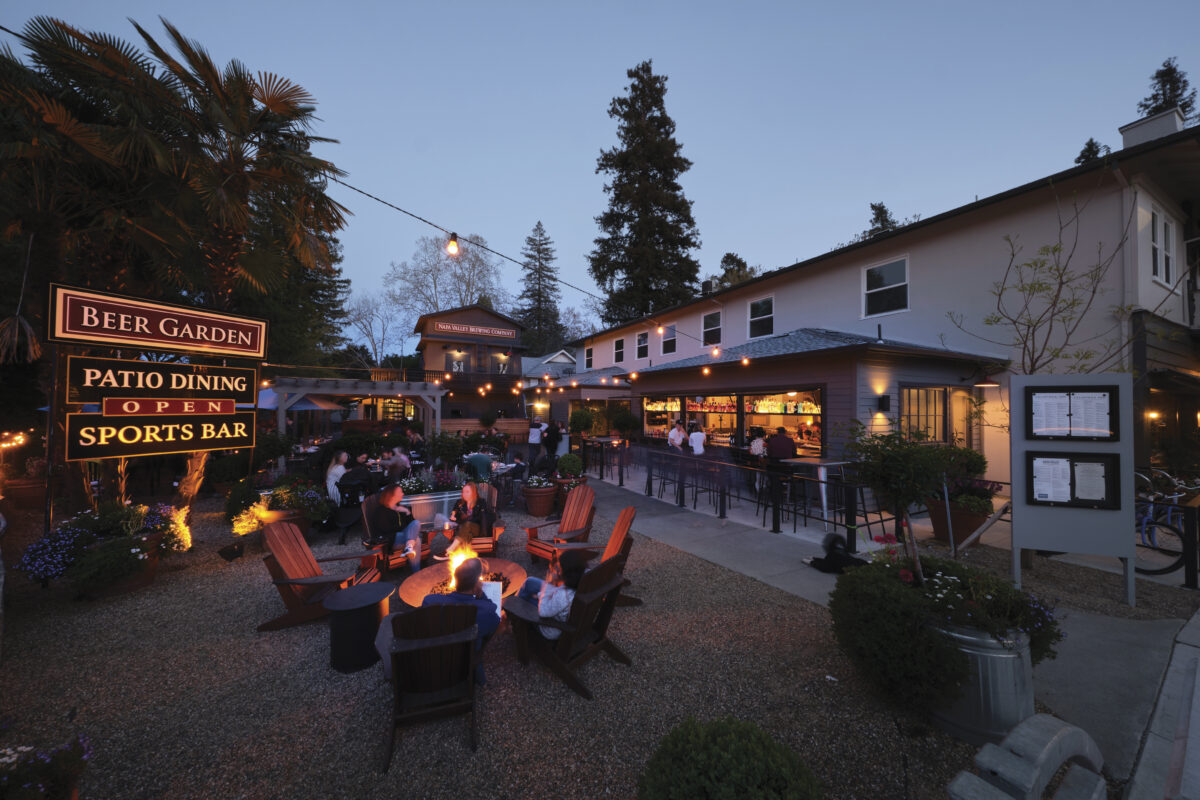 exterior view of Calistoga Inn at dusk with people sitting at firepit with string lights above for the article Taking Off The Chill 