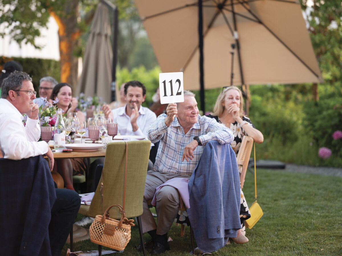 group of people at outdoor table with paddle up for an auction at OLE Health Foundation