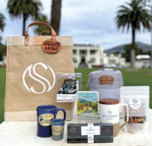 Silverado Resort bag, mug, cup, hat and other gifts on display outside on table with resort and palm trees in background for the article Holiday Gift Guide 