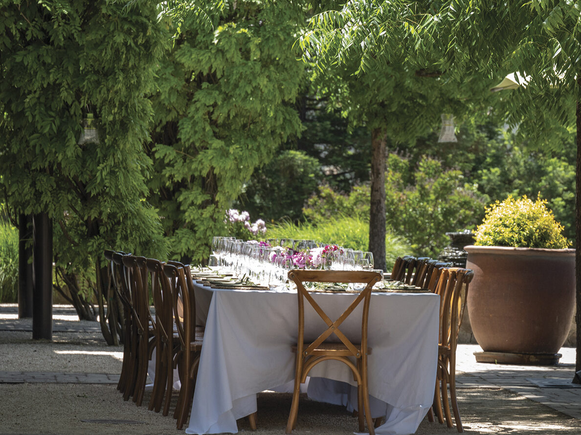 exterior courtyard at Somerston Estate Winery with green trees, a long table with white tablecloth and chairs