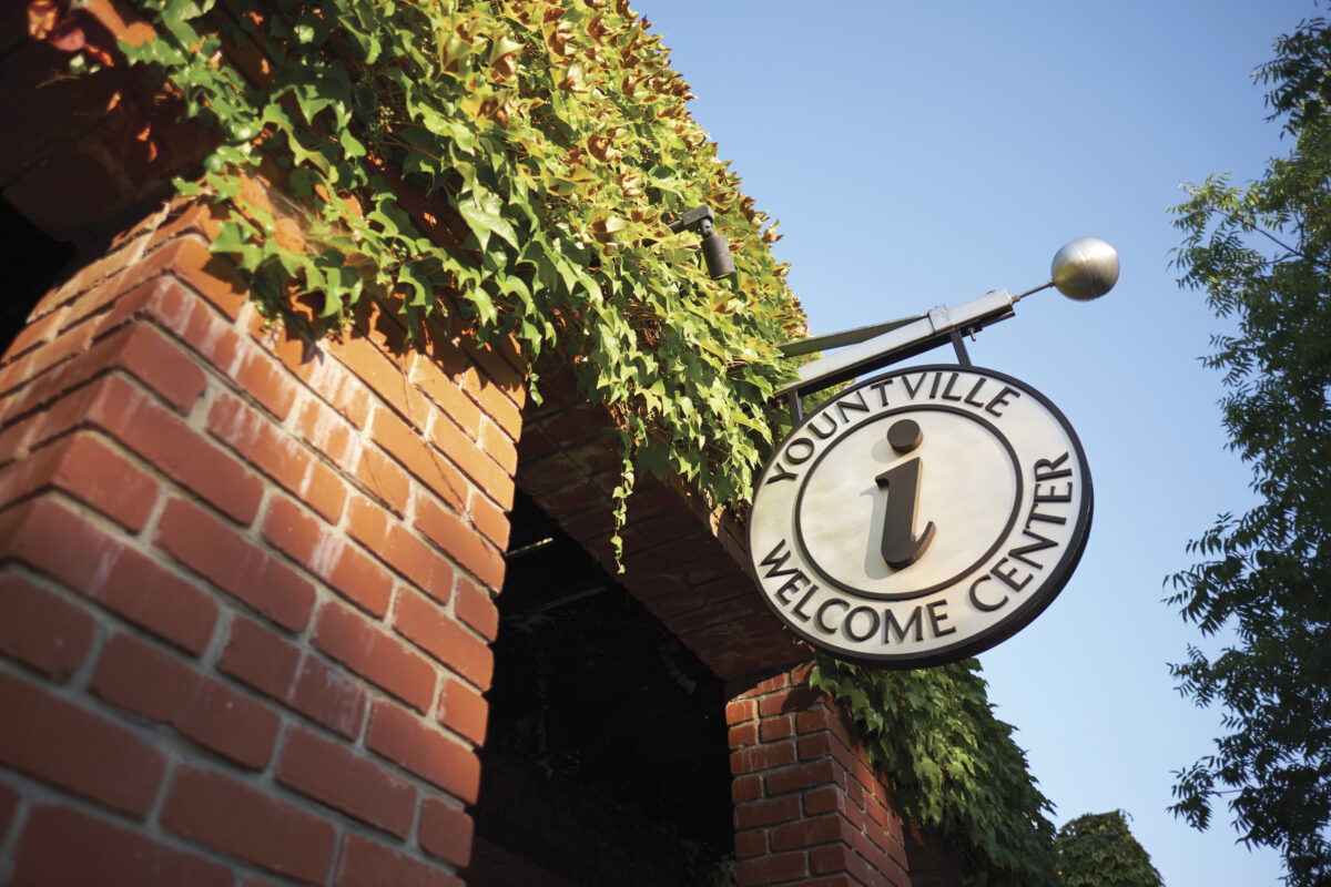 entrance of Yountville Welcome Center with signage over brick wall with vines growing on it