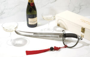 bottle of champagne and glass with champagne saber with red tassel and wood box