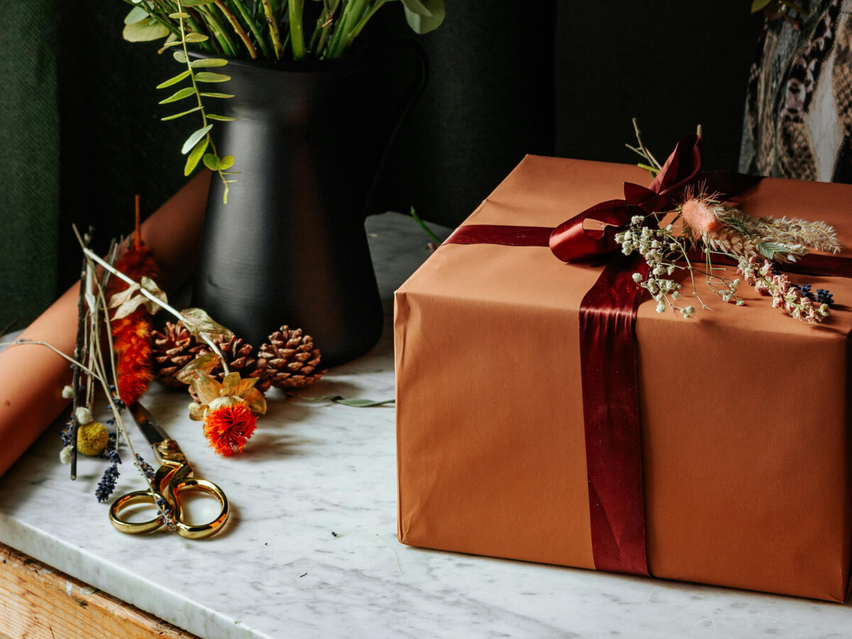 gift wrapped box on marble table with vase of flowers nearby and red ribbon for article Holiday Gift Guide