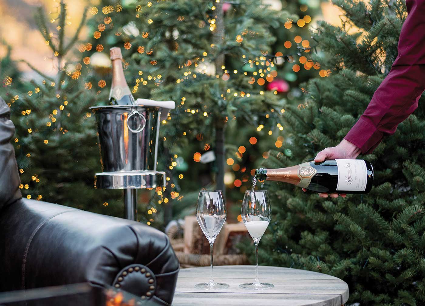 person pouring sparkling wine into flutes on outdoor table with holiday in decor in background at Four Seasons Winter Chalets at TRUSS Restaurant + Bar Napa Valley