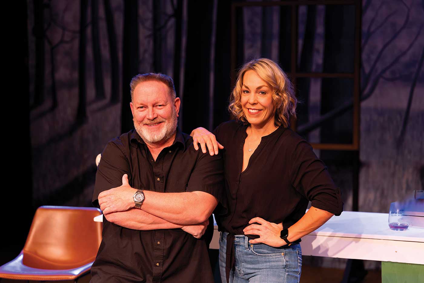 Barry Martin seated with arms crossed and Taylor Bartucci leaning with hand on hip and arm on shoulder with dark curtain behind them