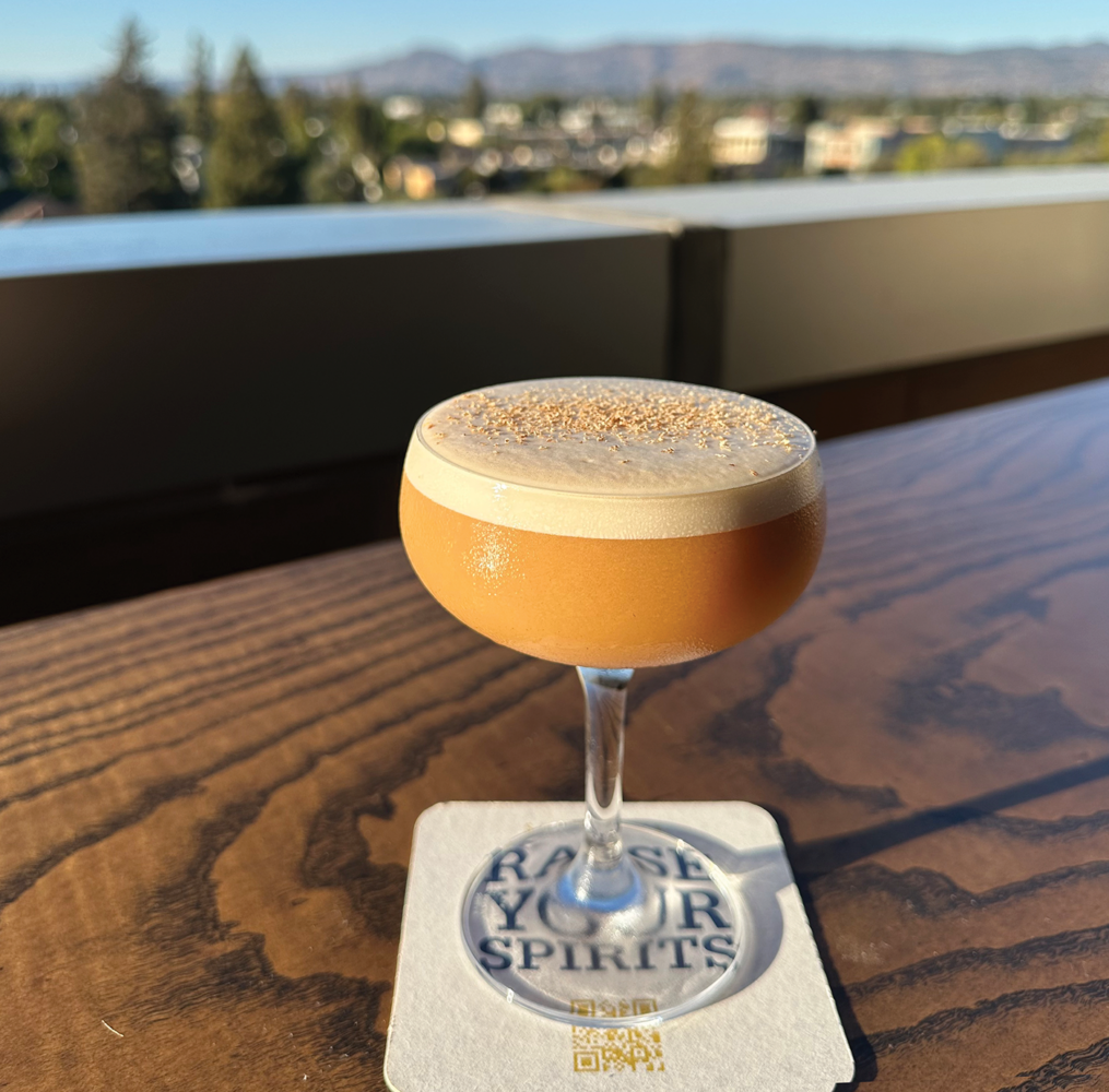 amber colored cocktail in clear coupe class on wooden table and coaster on outdoor table for seasonal sipping