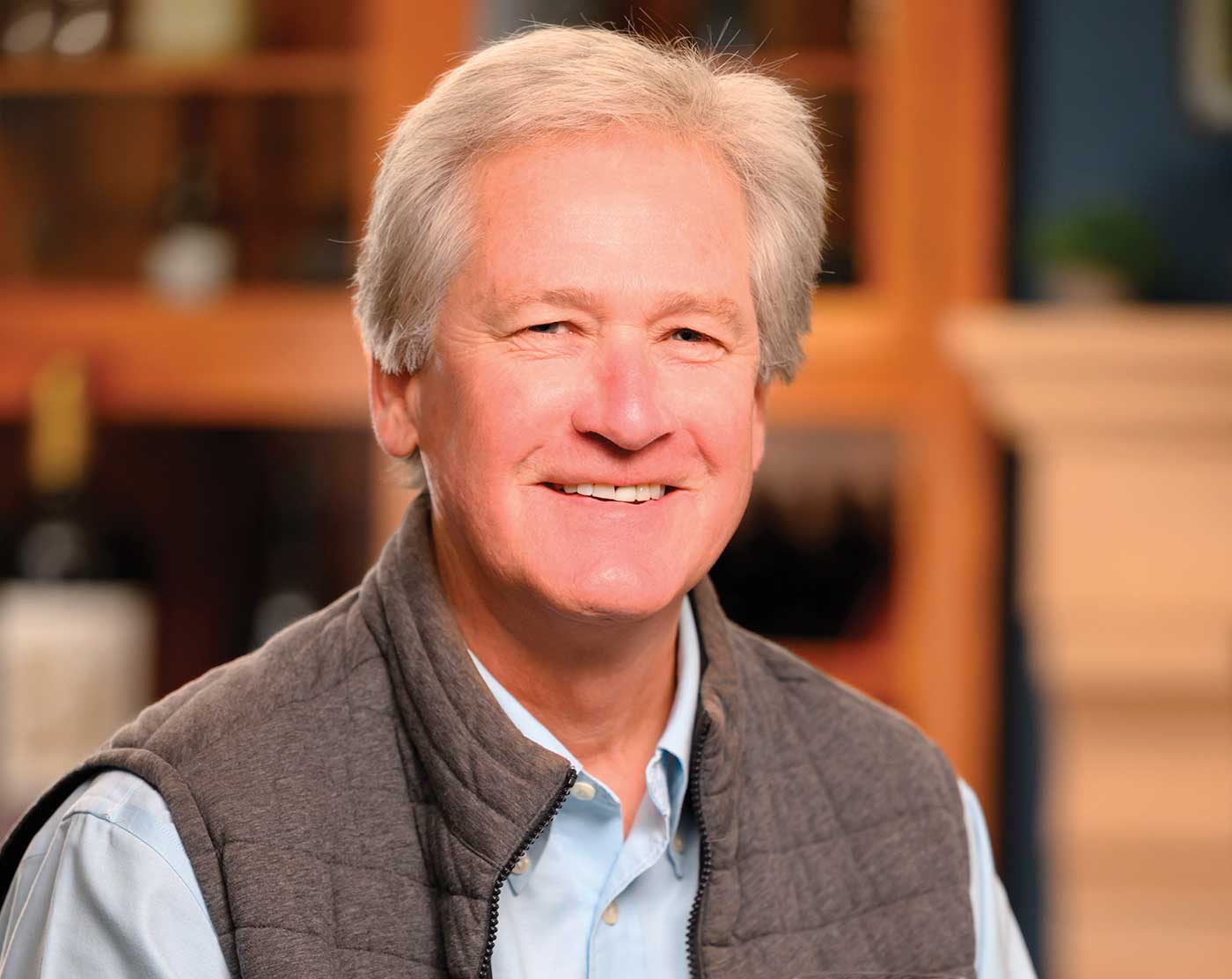 Judd Wallenbrock, indoors, wearing best over light blue button down shirt, smiling