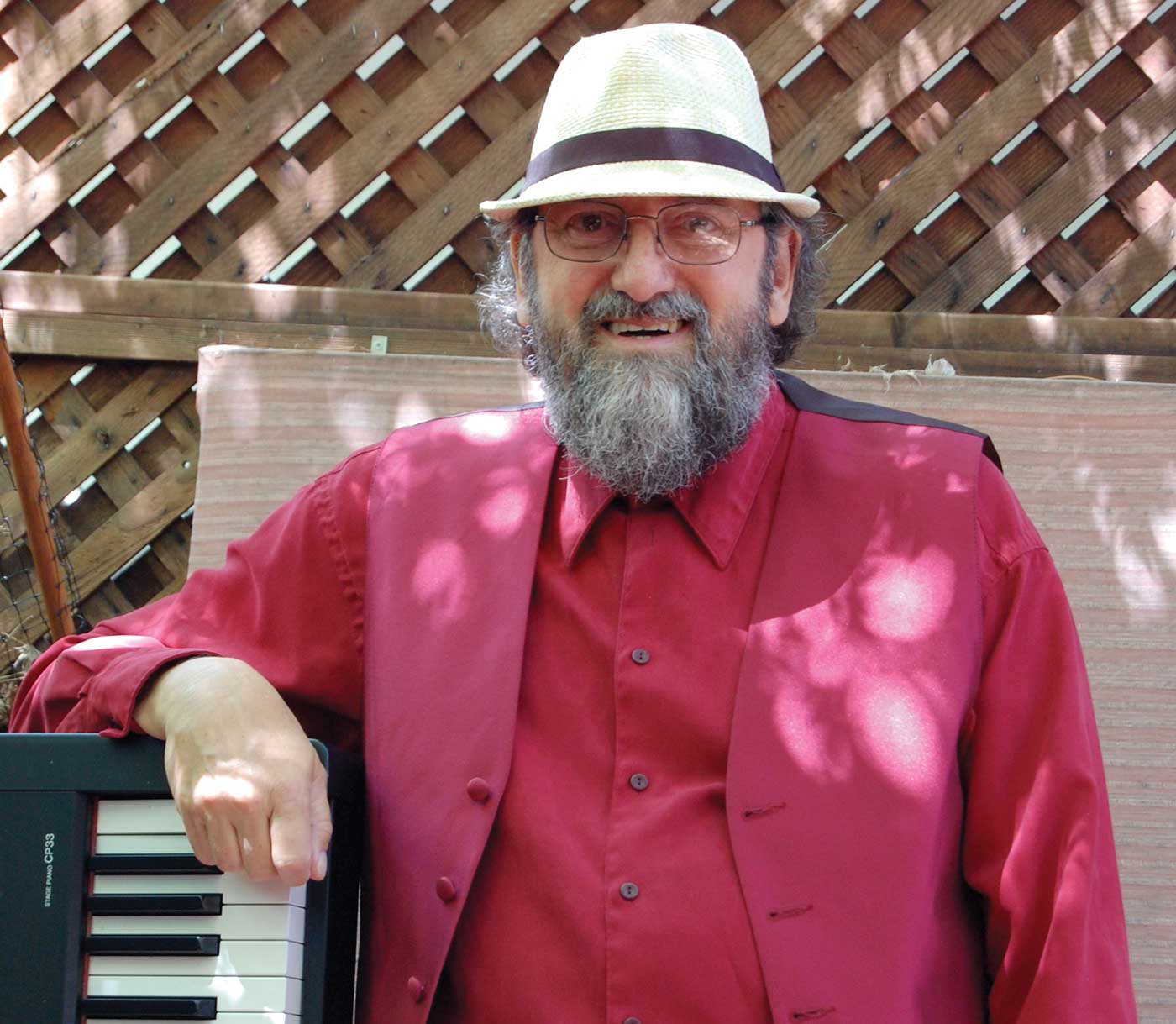 Mike Greensill leaning on keyboard outside wearing a red shirt, red vest and hat for Most Intriguing