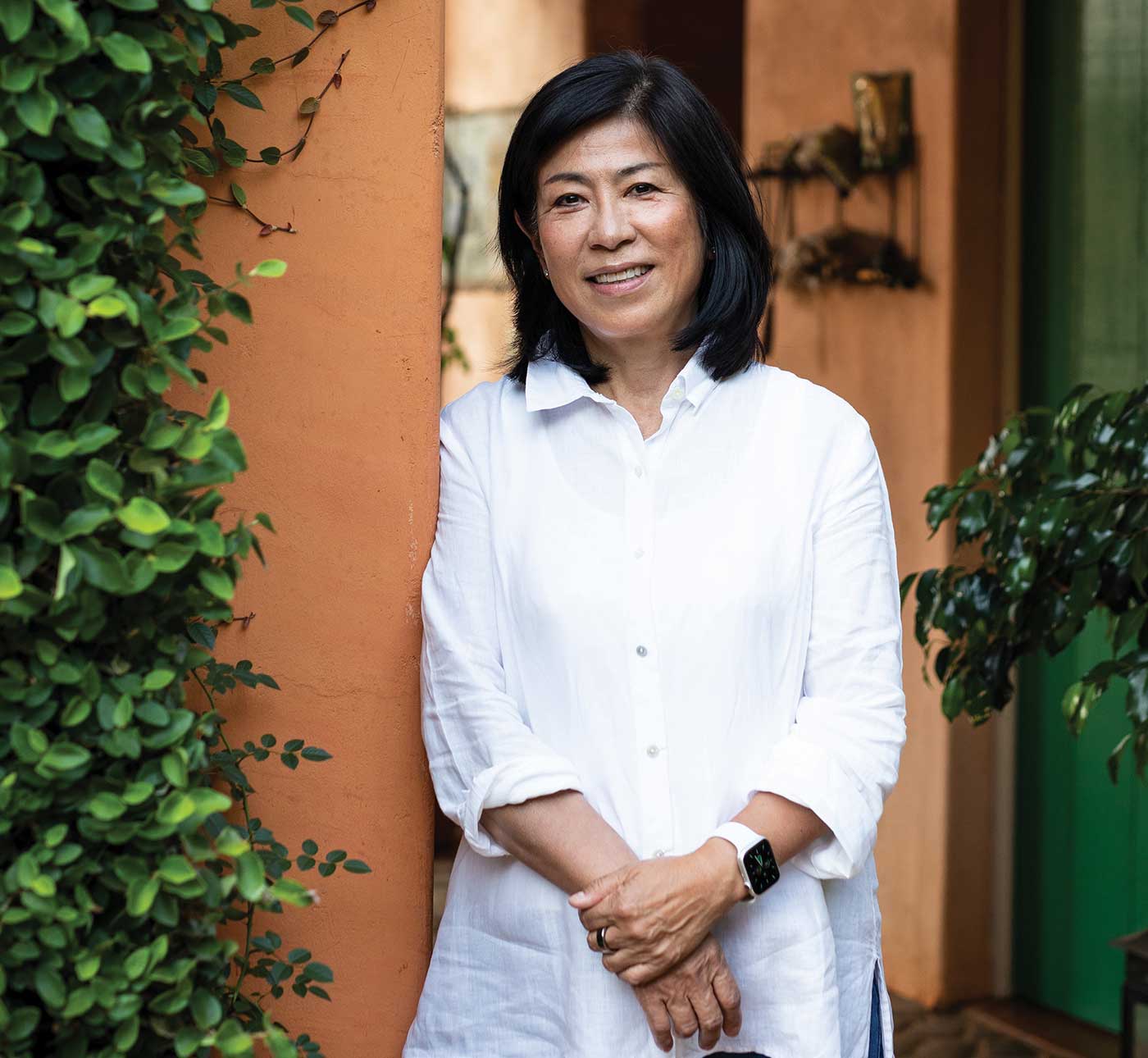 Naoko Dalla Valle standing outside, leaning on adove wall with greenery, wearing white shirt for 2024 Most Intriguing