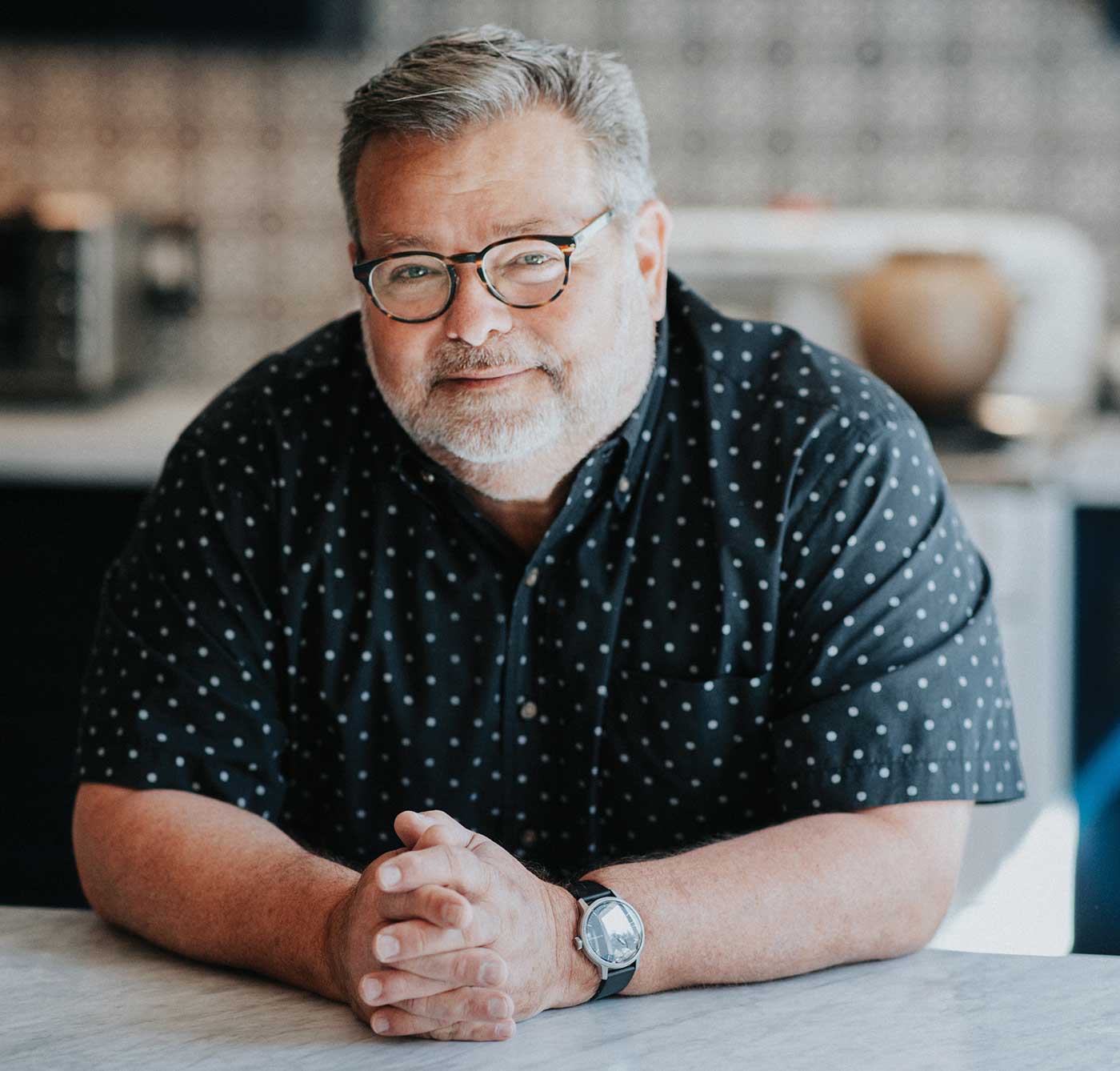 Steve Sando leaning on counter in kitchen, smiling wearing glasses