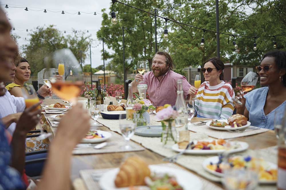 group of adults at outdoor table with food, holding wine glasses for toast