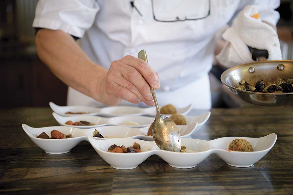 chef wearing apron filling bowls of food on wood table