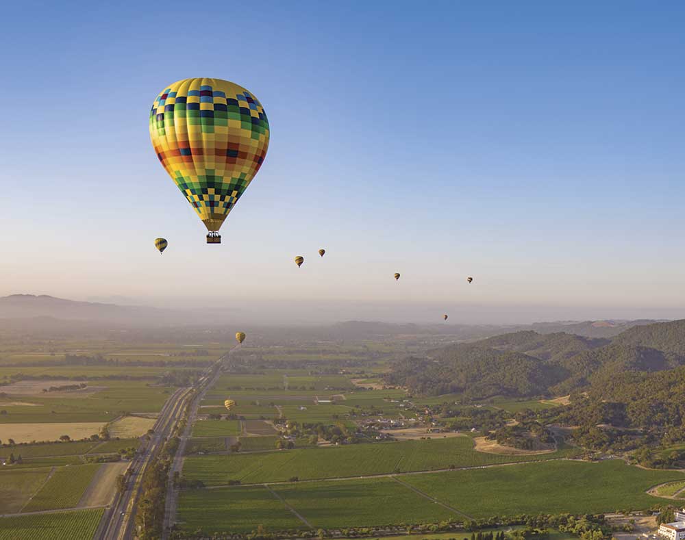 hot air balloons floating in the air over Napa Valley with blue sky