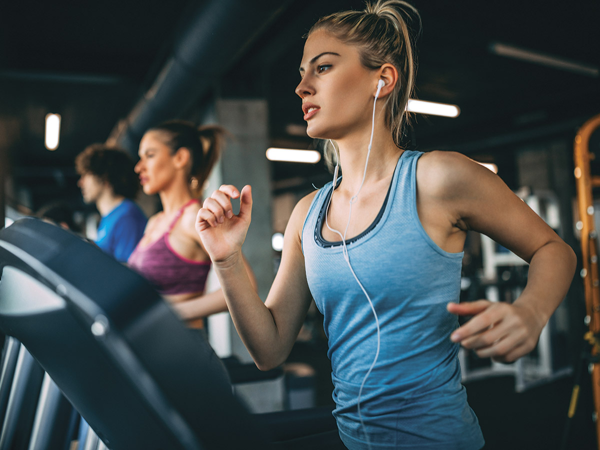 AdobeStock_200322386 people running on treadmills in gym with blond woman in blue tanktop in foreground for sweat stay fit shape article
