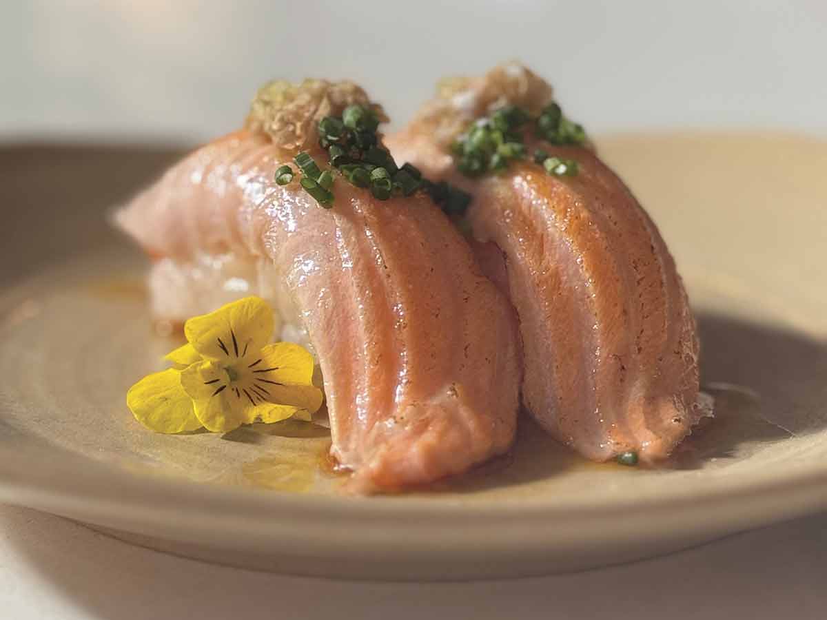 Photo–courtesy—of-Eikos 2 pieces of sushi on beige plate with yellow flower and chives on top for the Eikos story