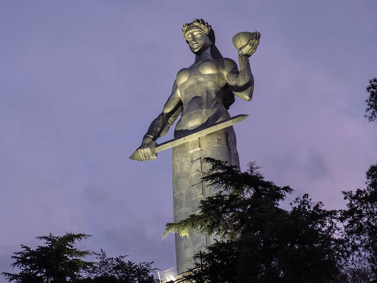 large statue of Kartlis Deda holding a pear and a sword with purple sky in background for Journey to Georgia article