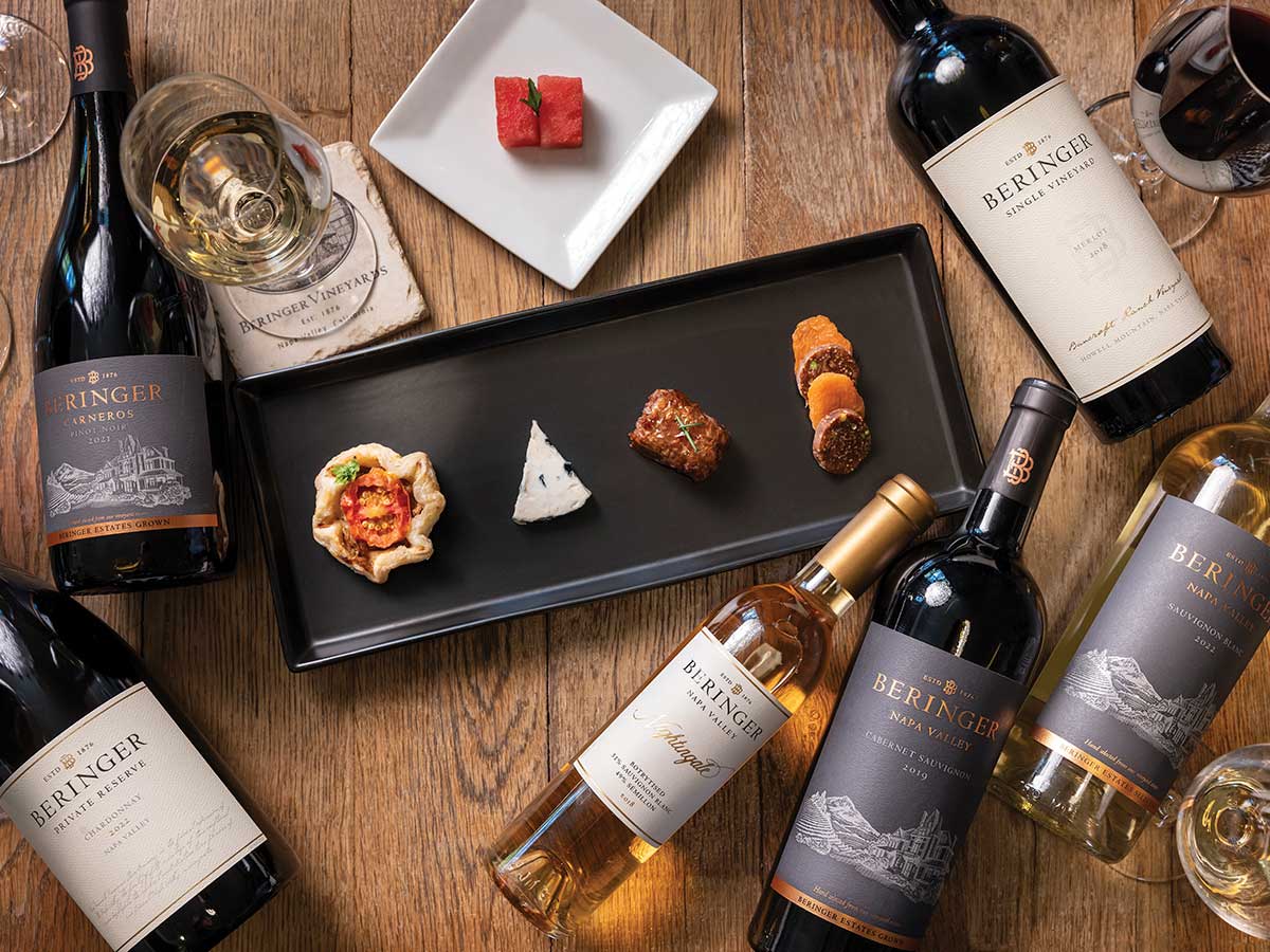 bottles of Beringer Vineyards wine displayed on a wooden table with plates of food
