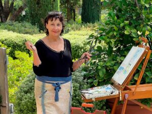 Napa Valley artist Nancy Willis standing at easel, holding paintbrush in garden for painting light article