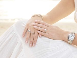 woman wearing white, seated with hands overlapped on knee, showing rings and watch for Blue Diamond Jeweler Article