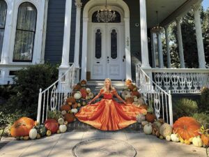 Allison Parks sitting on porch of navy house in orange gown with pumpkins placed about for Pumpkin Porch-scaping
