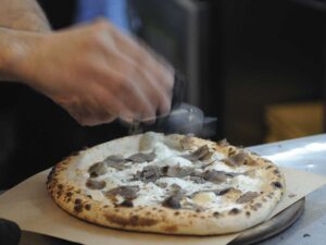 person sprinkling cheese on a pizza with truffles for the Napa Valley Truffle Festival article