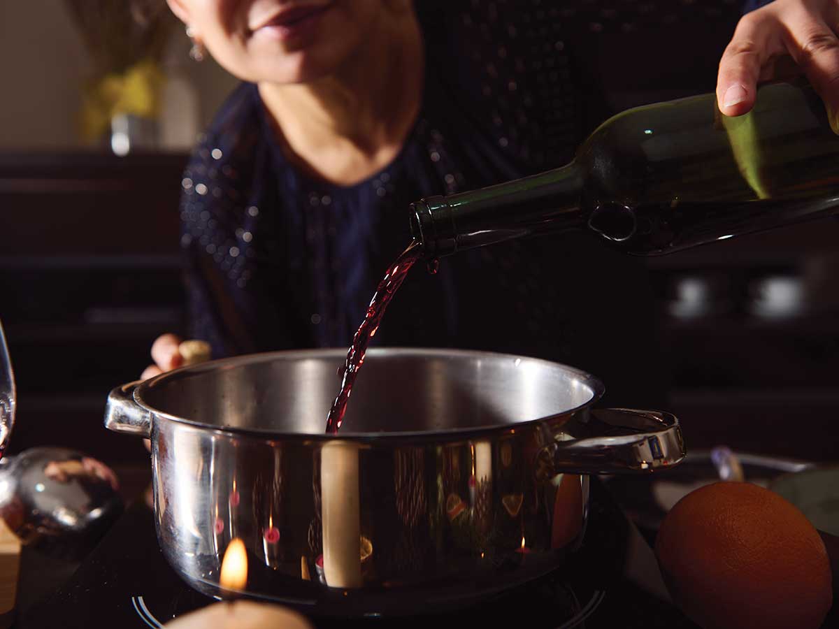 woman pouring Merlot into a pot while cooking for the Merlot: The Flavor Thread article